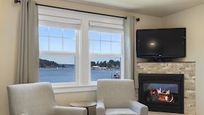 A living room with two armchairs, a television, and a fireplace with a visible fire. - Waterfront Inn (Gig Harbor)