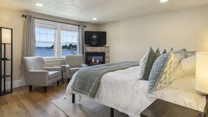 A bedroom with a fireplace, a bed, a TV, and a view of the outdoors. - Waterfront Inn (Gig Harbor)