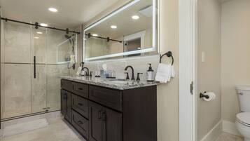 A modern bathroom with a glass-enclosed shower, dark cabinetry, a large mirror, and a toilet.