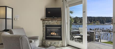 A living room with a stone fireplace, a flat-screen TV, and a view of a lake and dock.
