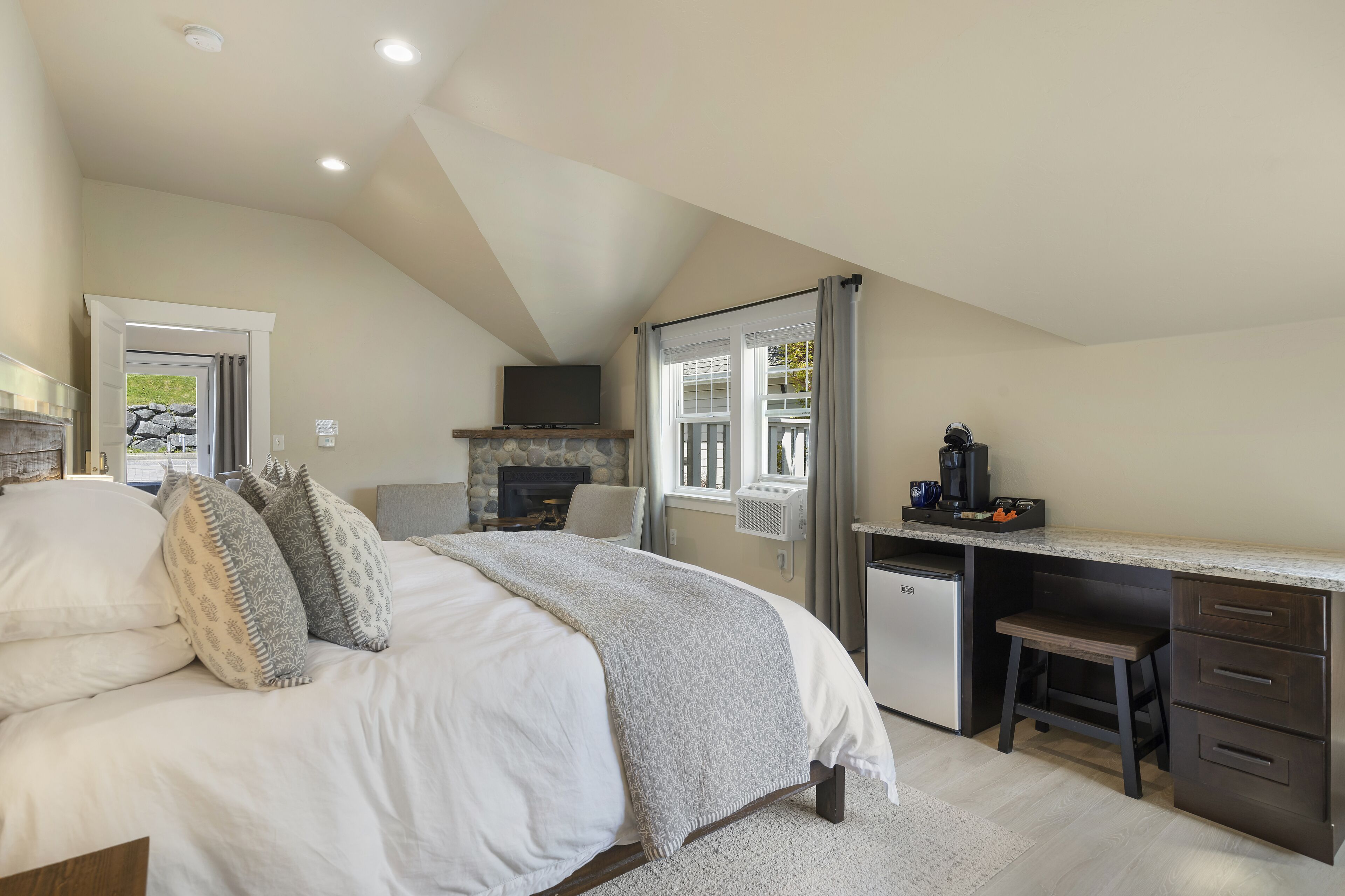 A bedroom with a bed, a desk, a fireplace, and a window.