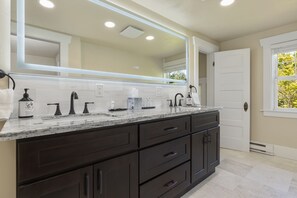 A bathroom with a large mirror, dark cabinetry, a marble countertop, and a white door.