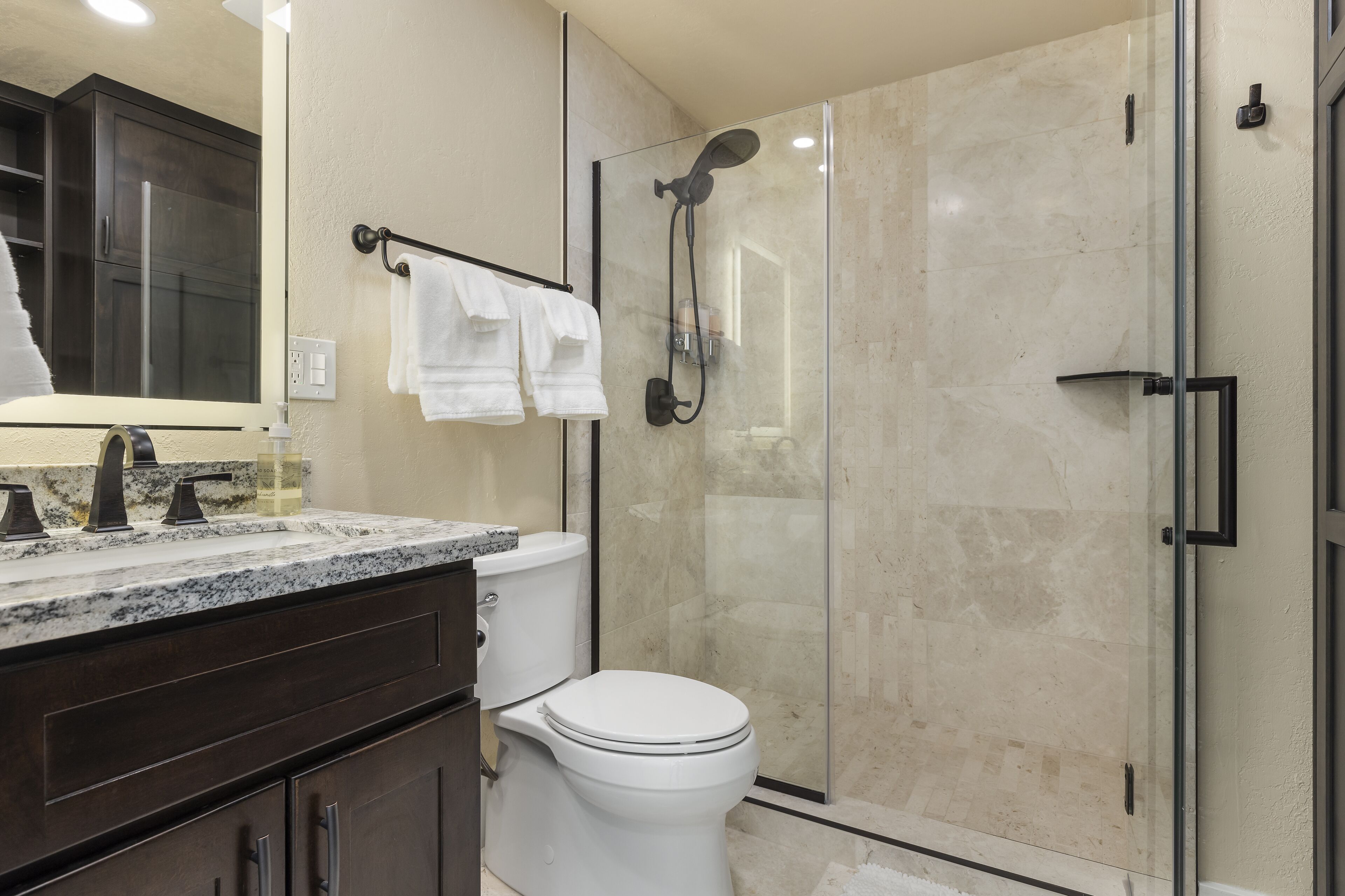 A modern bathroom with a glass-enclosed shower, a white toilet, and a marble countertop.