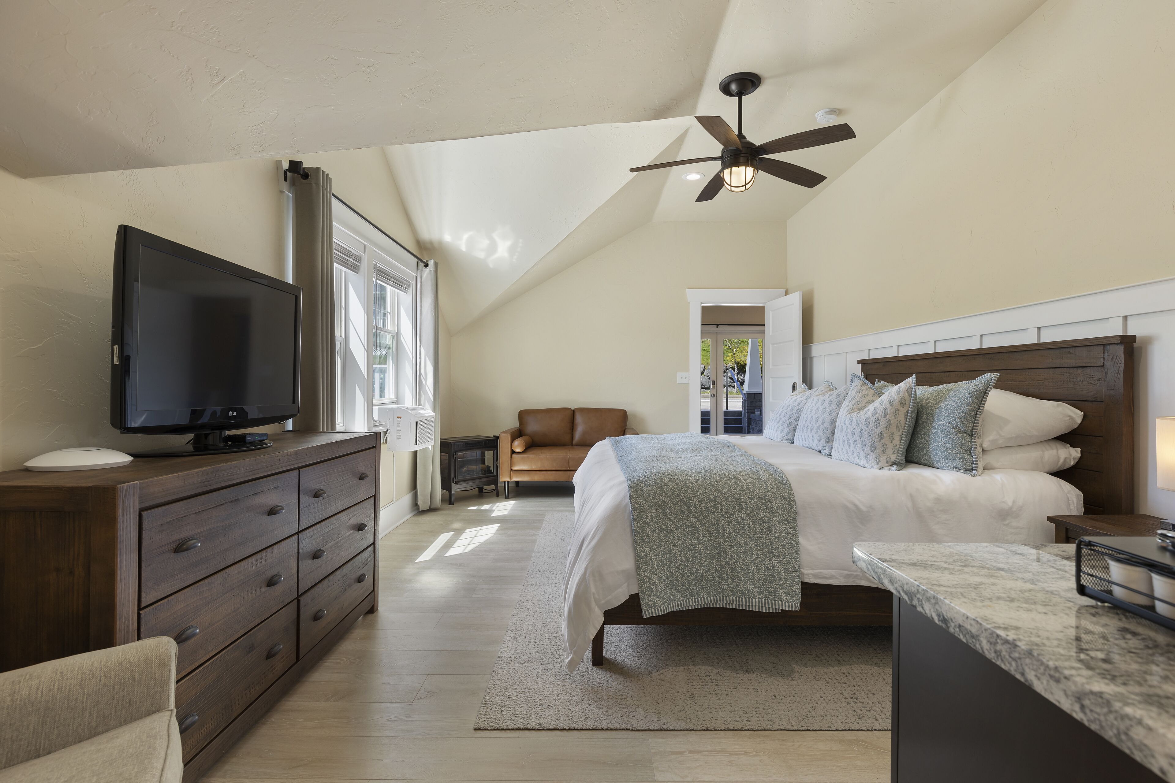 A bedroom with a bed, a TV, a dresser, and a ceiling fan.