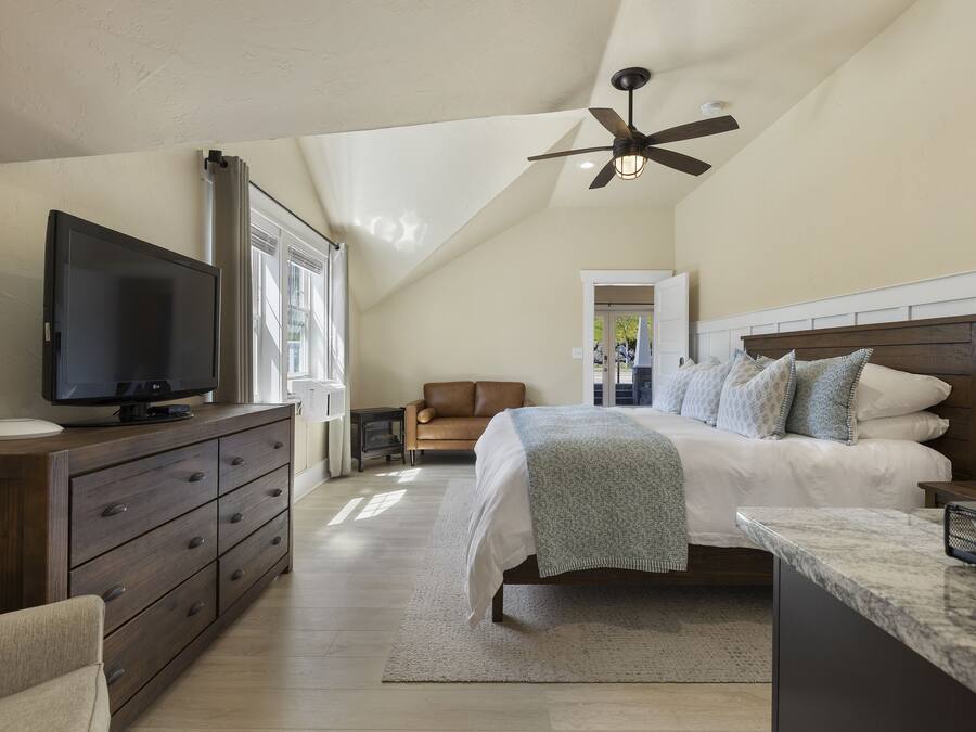 A bedroom with a bed, a TV, a dresser, and a ceiling fan.