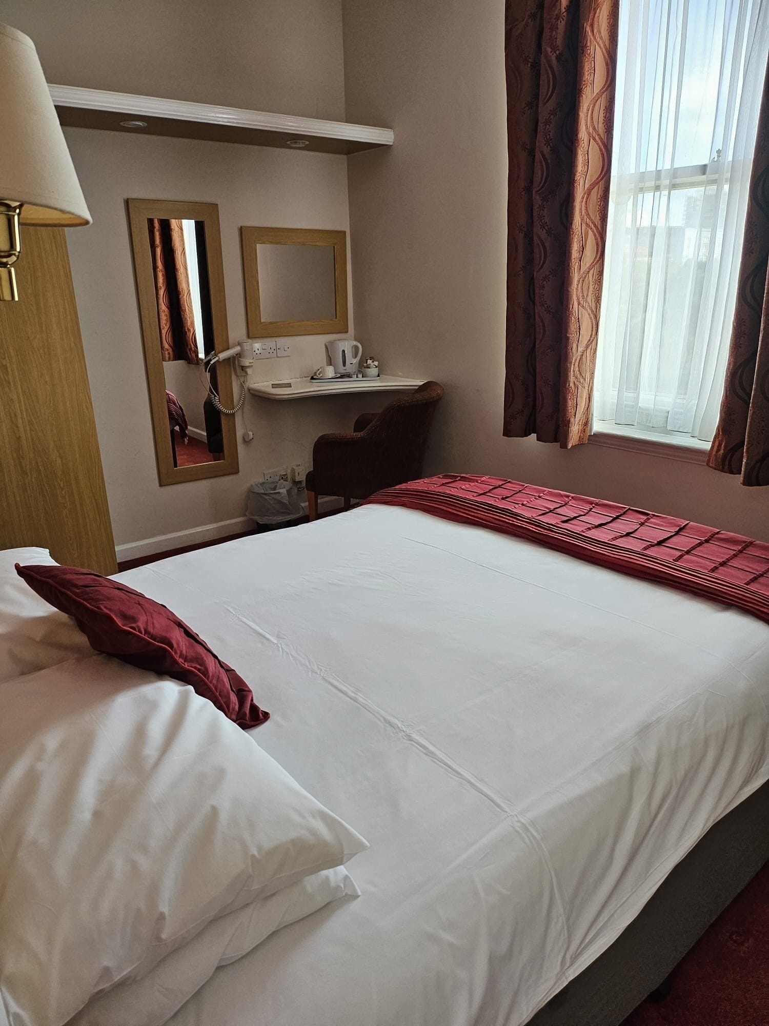 A hotel room with a bed, a desk, a mirror, and a window with curtains.
