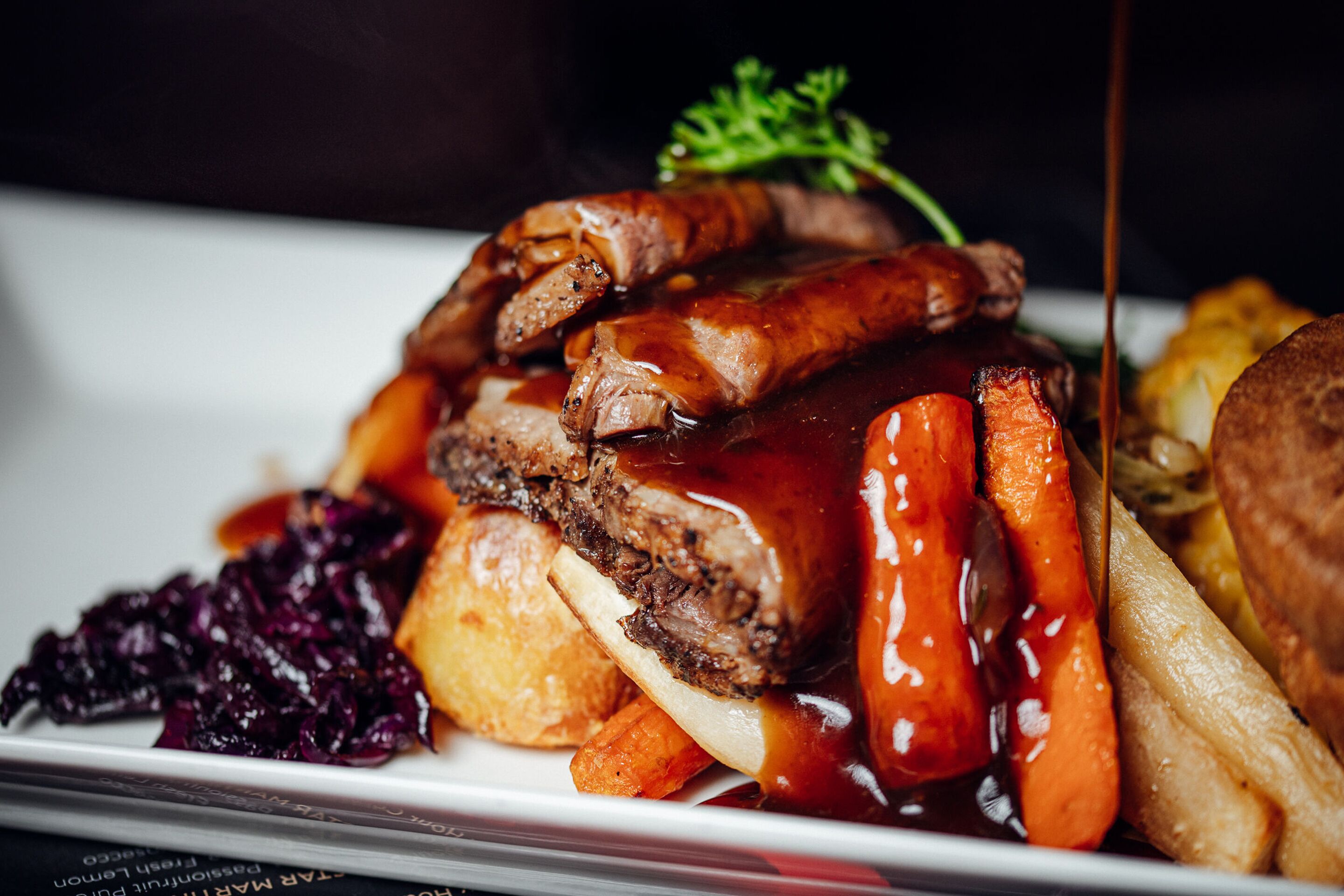 A plate of food with roast beef, sausages, and vegetables.