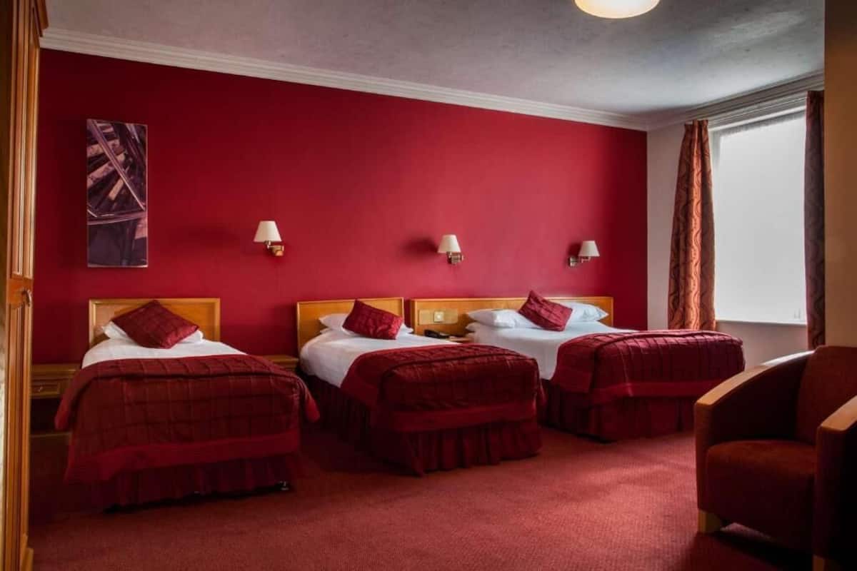 Een hotelkamer met drie bedden, rode wanden en een groot raam met gordijnen.