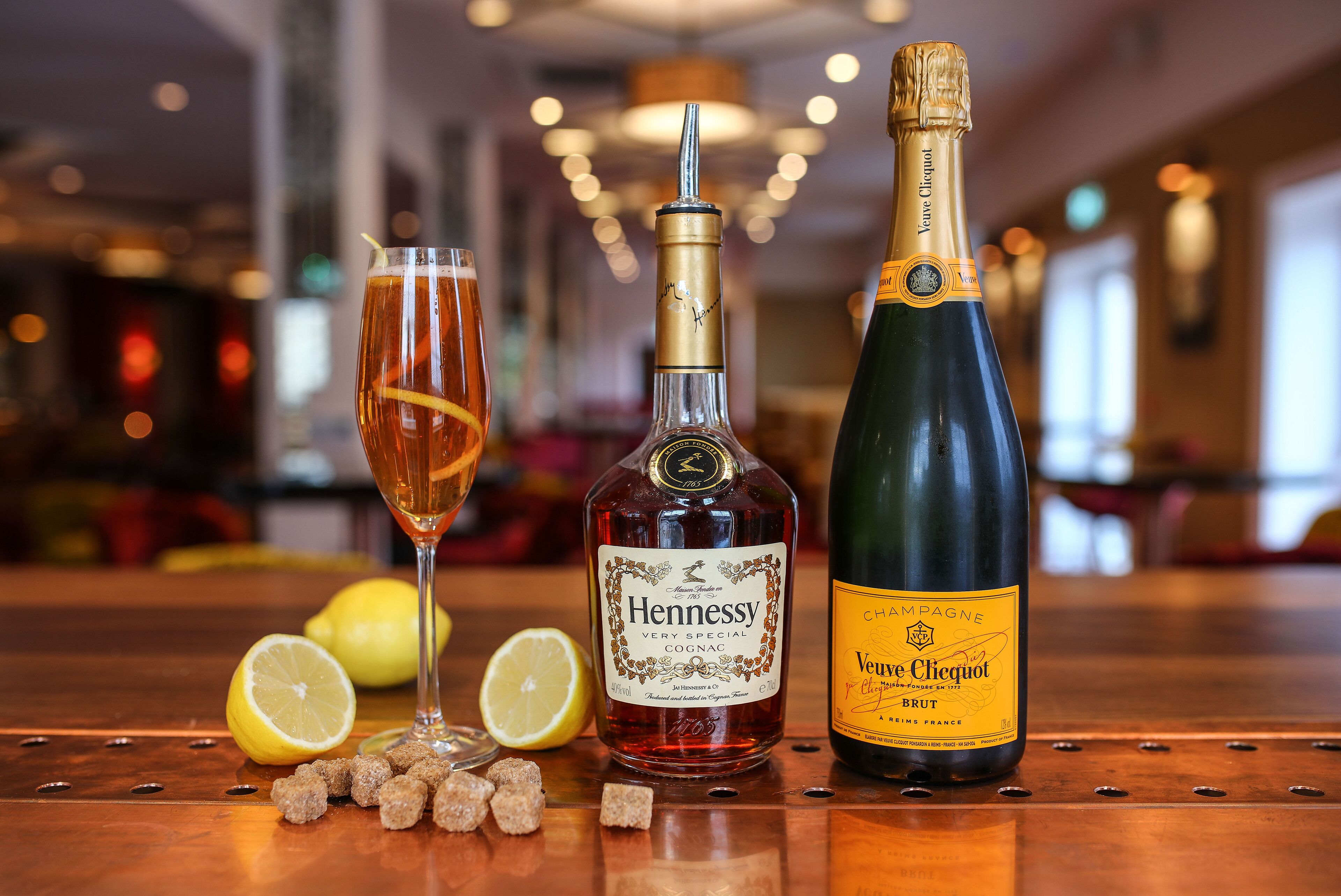 Un bar con una botella de Cognac Hennessy, una botella de champagne Veuve Clicquot Brut y una copa de cóctel adornada con limón.