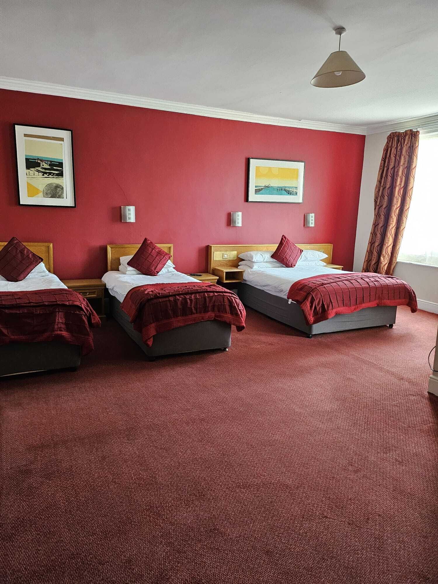 A hotel room with three beds, red walls, and artwork on the walls.
