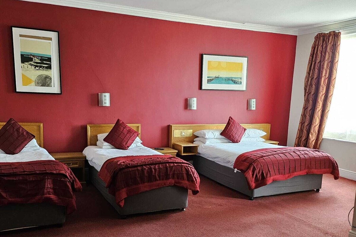 A hotel room with three beds, red walls, and artwork on the walls.