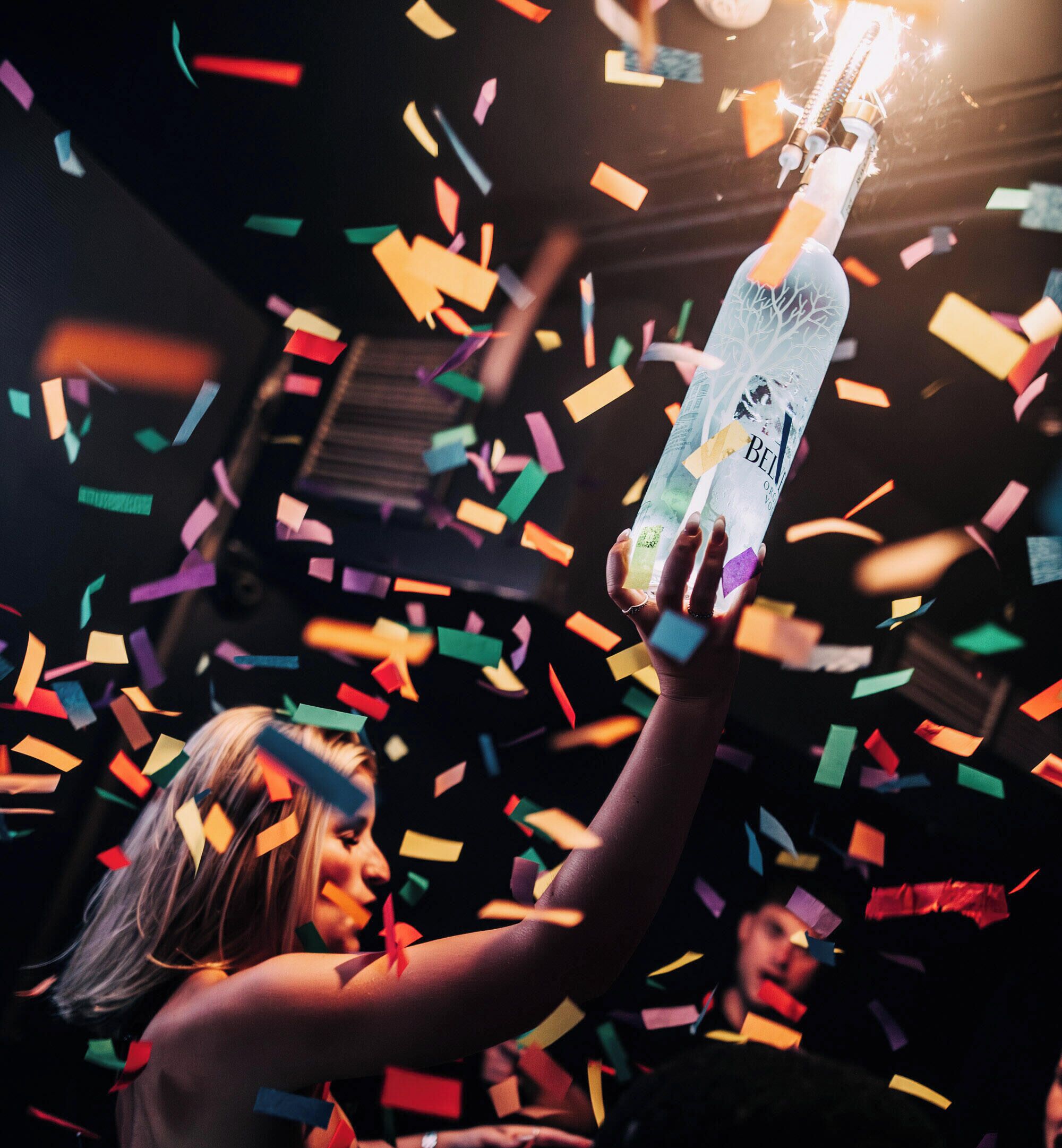 A person holding a bottle with a tree design, surrounded by colorful confetti.
