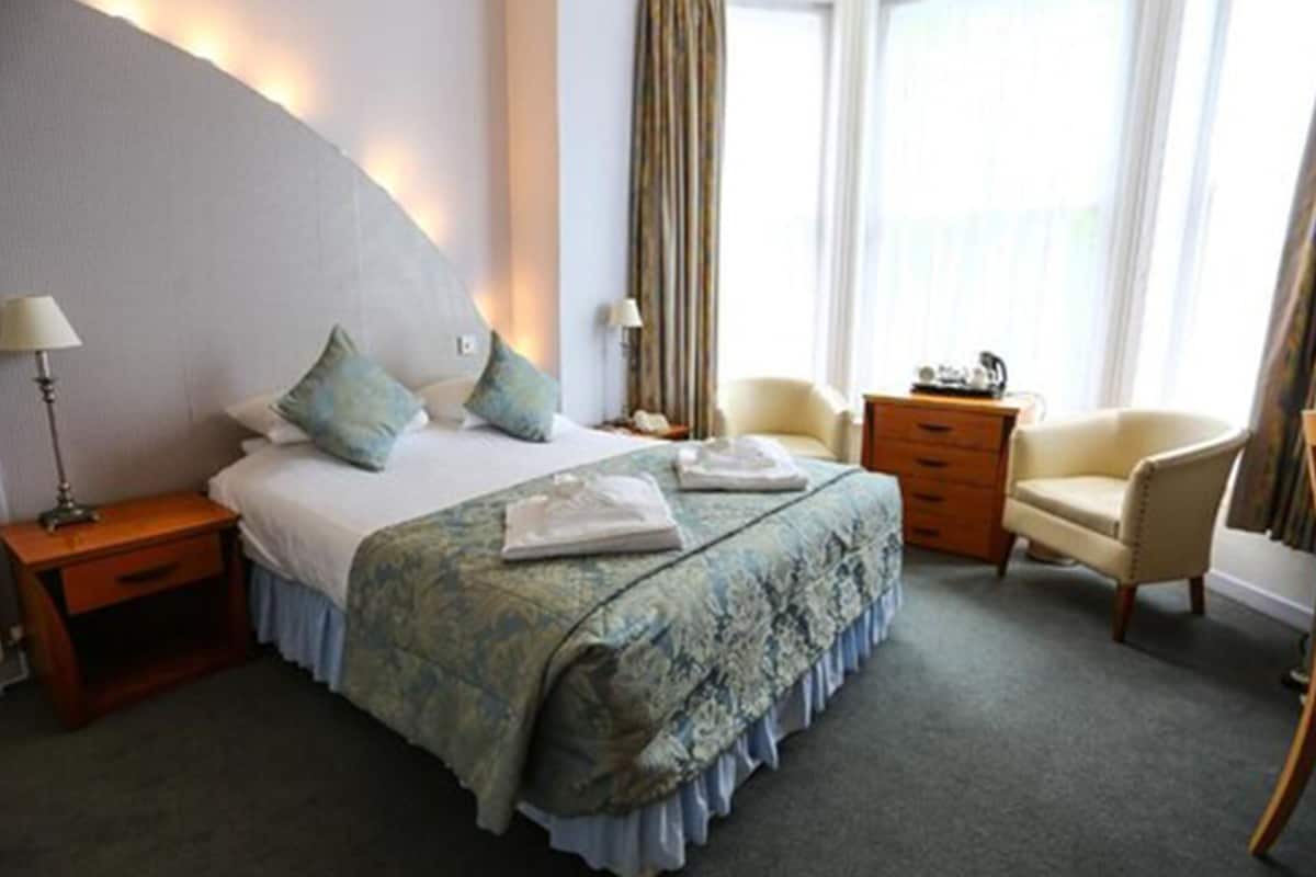 Ein Hotelzimmer mit einem großen Bett, einem Nachttisch, einem Sessel und einem Schreibtisch.