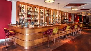 A bar with a wooden counter, multiple shelves of liquor bottles, and several bar stools. - Royal Exeter Hotel (Bournemouth)