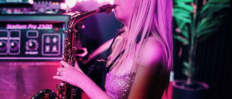 A person playing a saxophone in a room with a neon sign in the background.