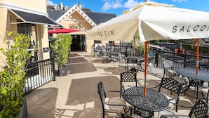An outdoor patio with black metal tables and chairs, a white umbrella with 'SALCONB' branding, and a building entrance with 'SALCONB' signage. - Royal Exeter Hotel (Bournemouth)