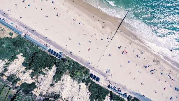 An aerial view of a beach with people, umbrellas, and a road running parallel to the shore. - Royal Exeter Hotel (Bournemouth)