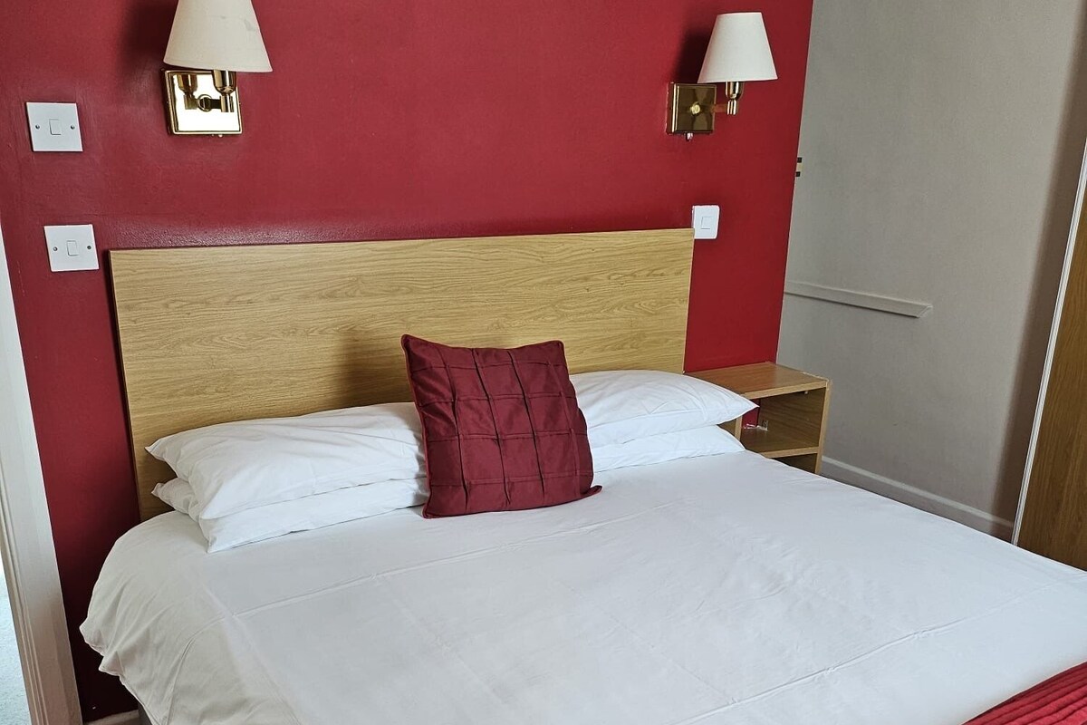 A hotel room with a bed, two bedside lamps, a nightstand, and a door.