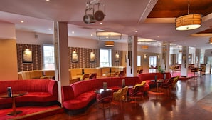 A spacious lobby with red seating areas, multiple tables, and large windows providing natural light. - Royal Exeter Hotel (Bournemouth)