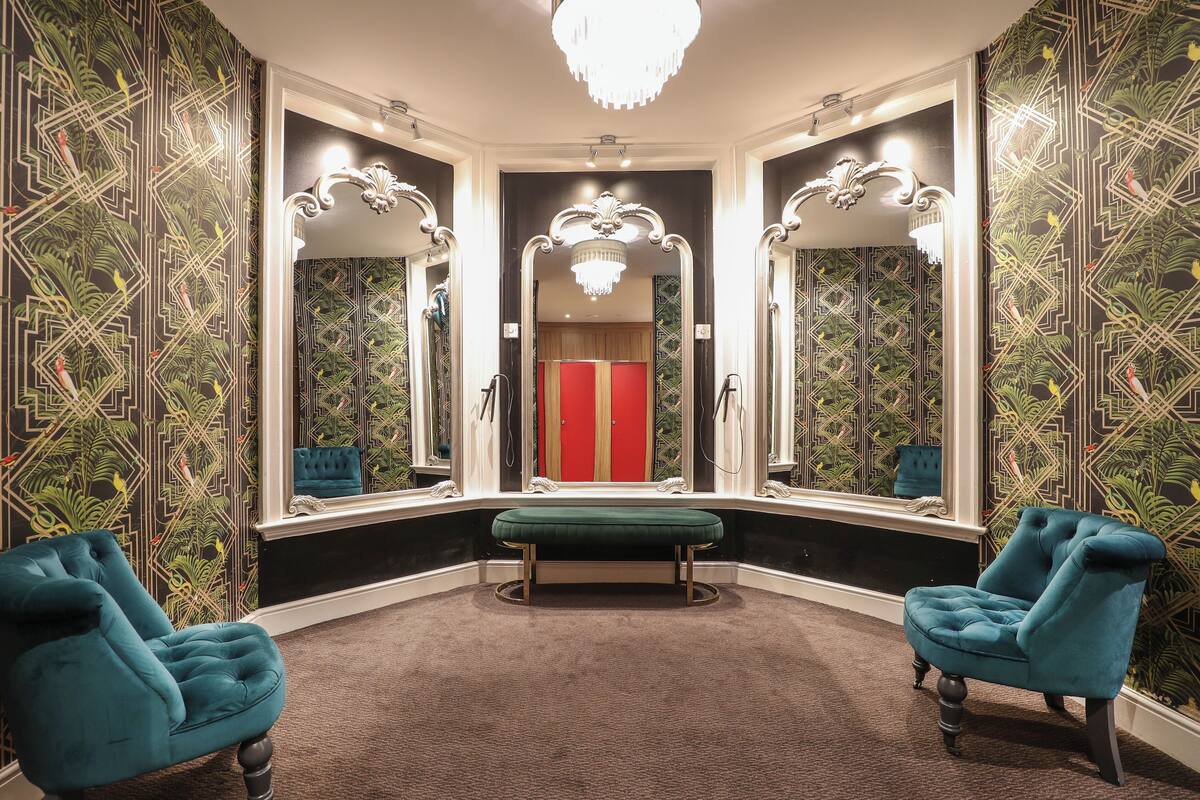 Een hoekzaal met een groene bank, twee blauwe fauteuils en een rode deur op de achtergrond.