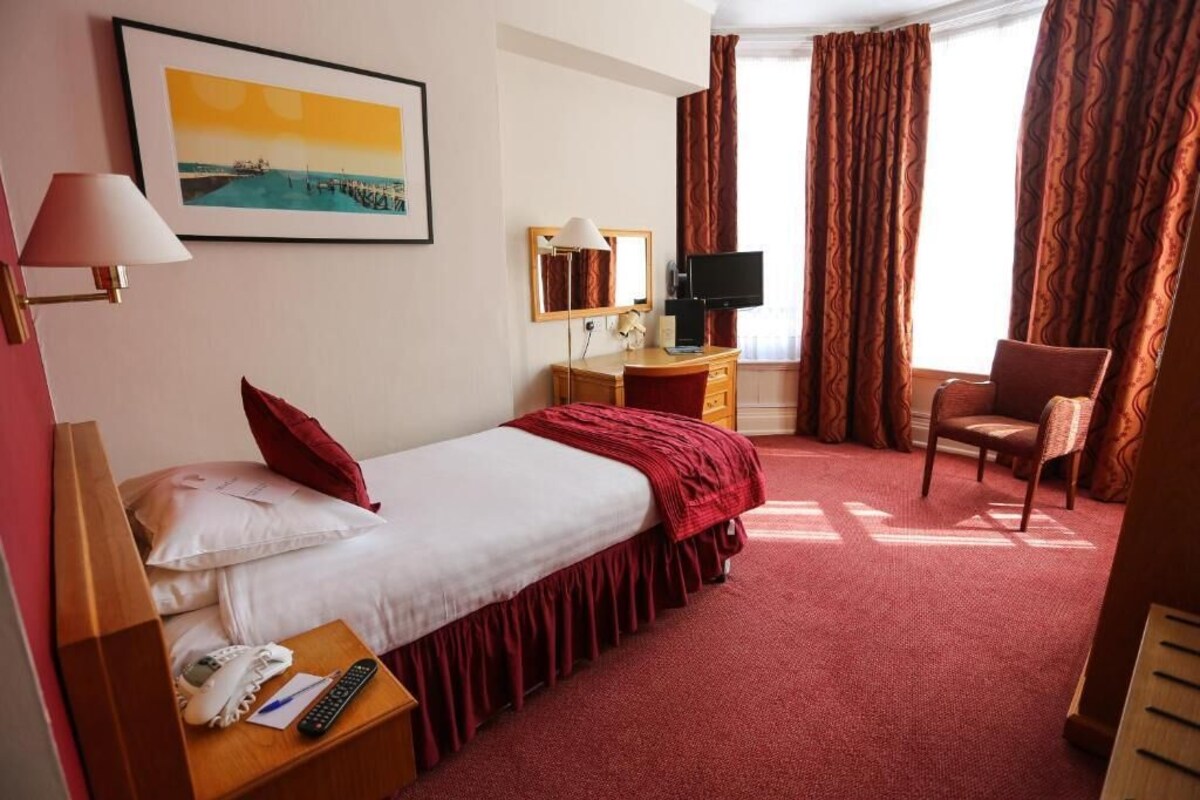 A hotel room with a bed, a desk with a lamp, a television, and a chair.