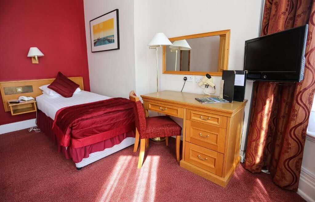 Een hotelkamer met een bed, een bureau met stoel, een televisie en een lamp.