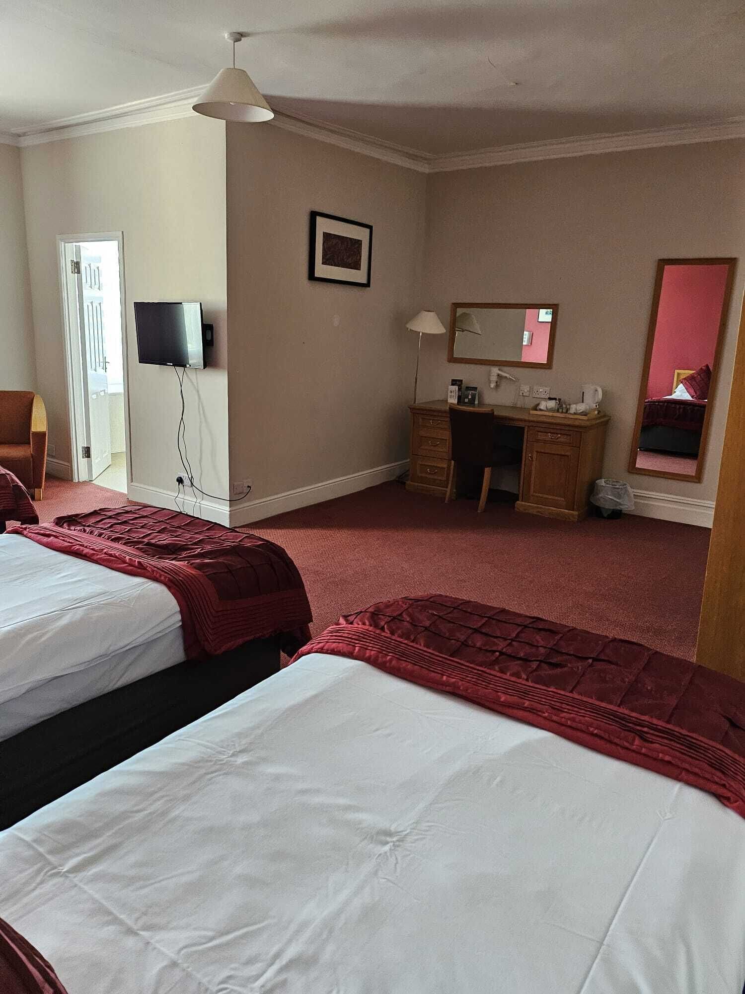 A hotel room with two beds, a desk, a chair, a television, and a mirror.