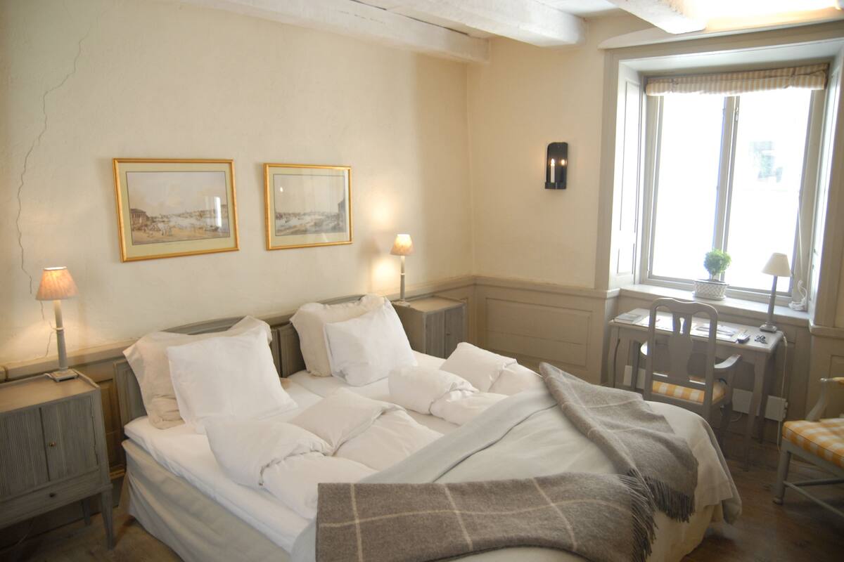 A neatly made bed with white linens, a bedside table with a lamp, and two framed pictures on the wall.