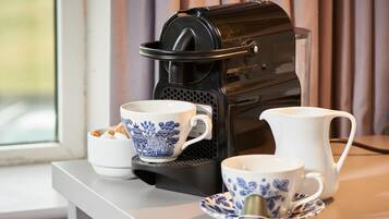A coffee maker, two cups with blue floral designs, and a white pitcher on a table near a window.