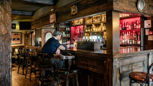 A bar area with wooden furniture, a bartender, and shelves stocked with bottles.