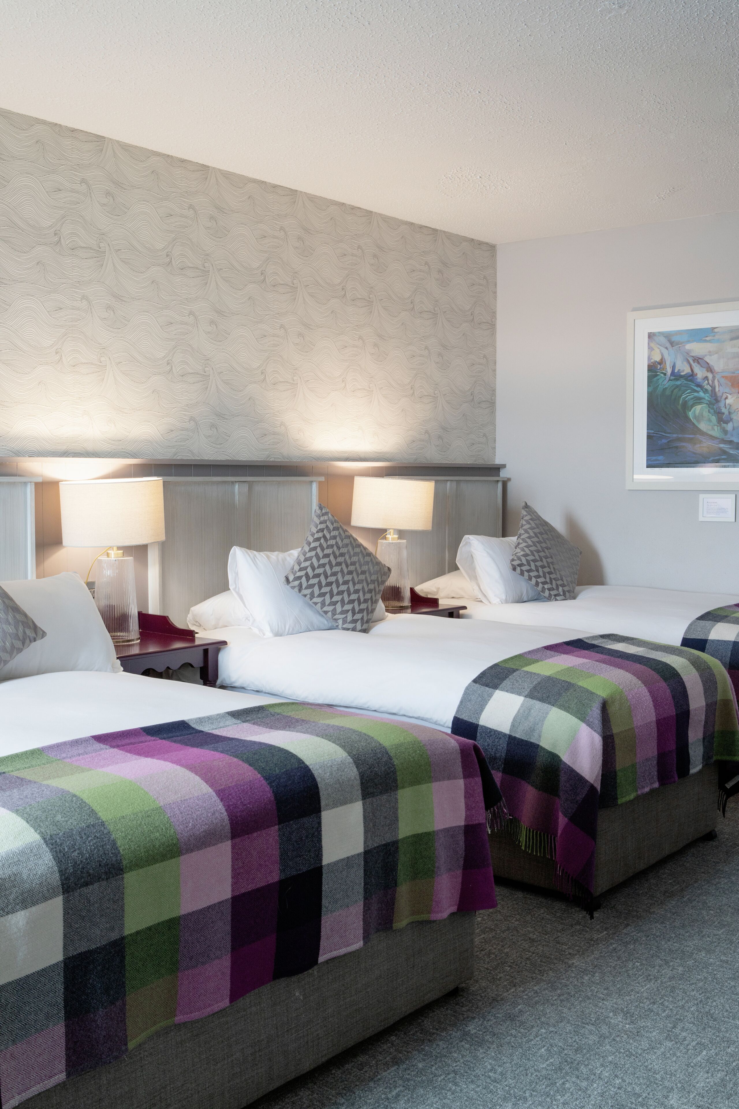 A hotel room with two beds, each with a checkered blanket, bedside lamps, and a headboard.