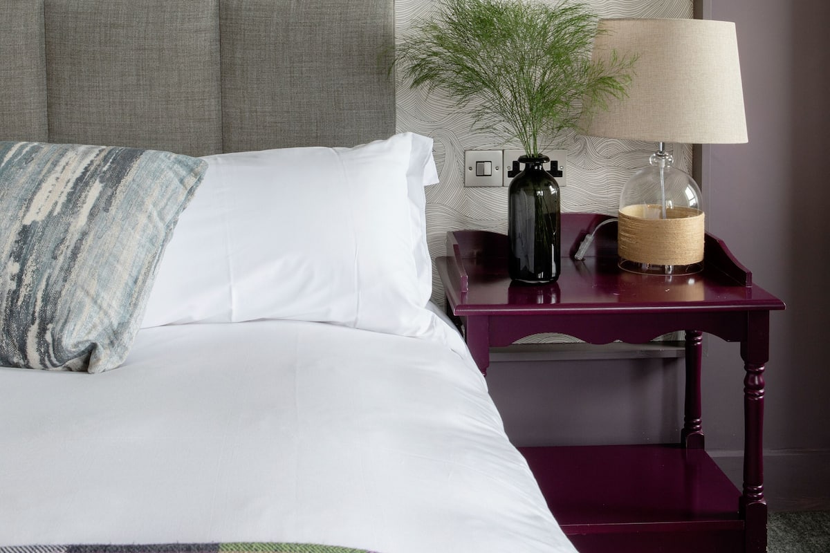 A neatly made bed with a checkered blanket, a bedside lamp, and a decorative vase on a nightstand.