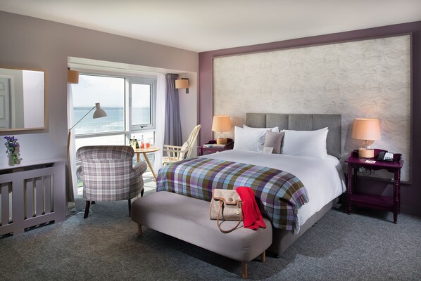 Une chambre d’hôtel avec un grand lit, une chaise, une petite table et une vue sur l’océan.