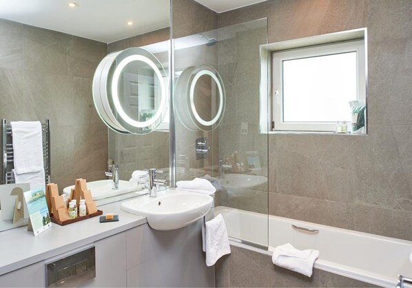 Un baño moderno con un espejo grande, dos espejos redondos, un lavamanos, una bañera y una ventana.