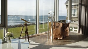 A room with a large window overlooking a coastal view, a tripod, and a copper bathtub.