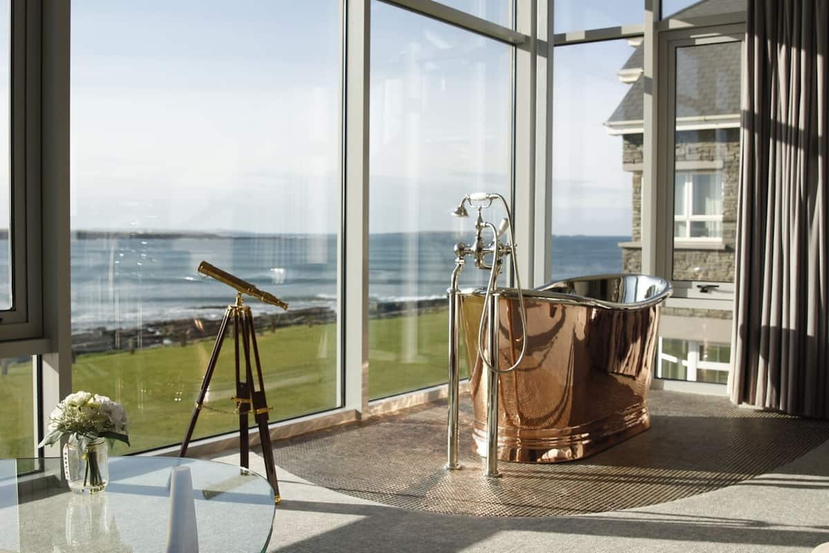 A room with a large window overlooking a coastal view, a tripod, and a copper bathtub.