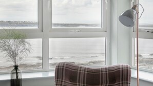 A plaid armchair by a window with a view of the sea.