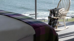 A bedroom with a large window overlooking a body of water, a bed, and a rocking chair.