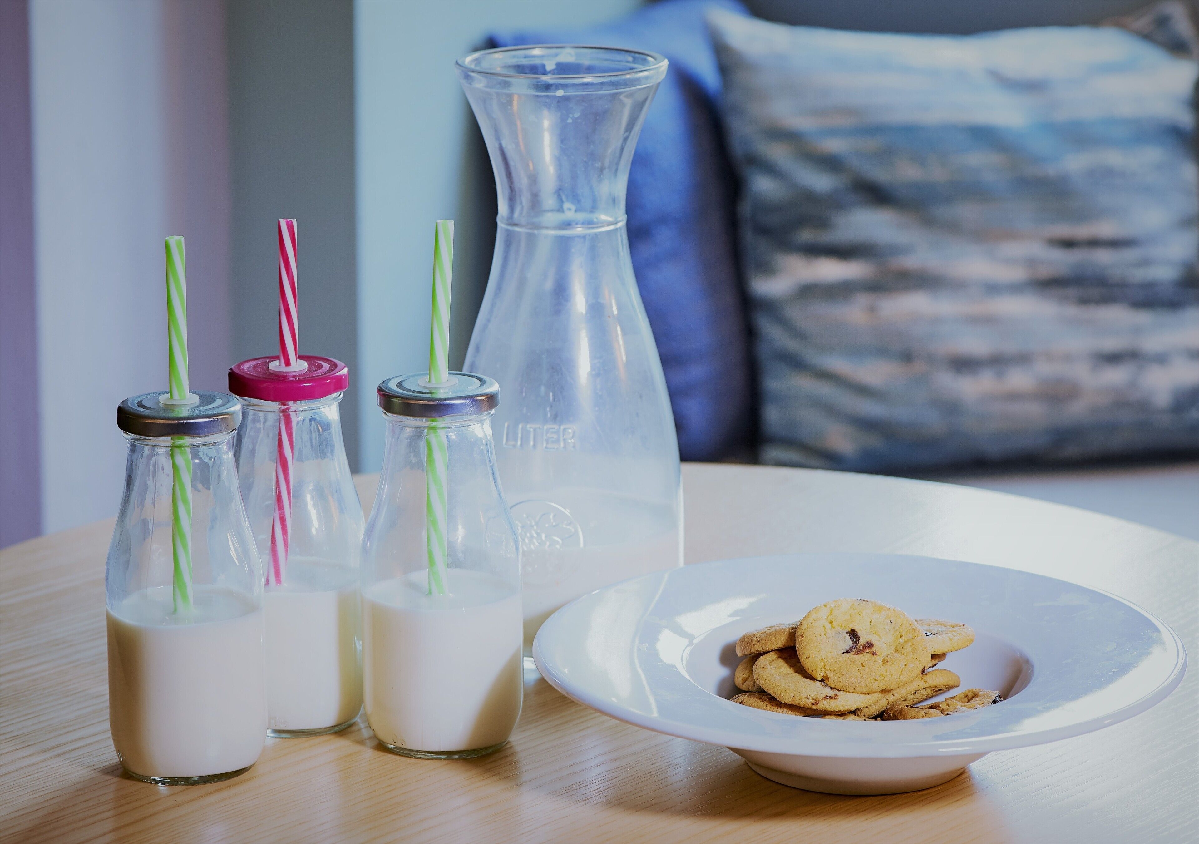 A table with three milk bottles, a large water bottle, and a plate with cookies.
