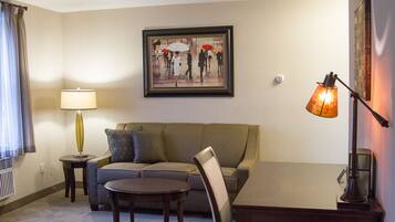 A hotel room with a sofa, two chairs, a small table, a lamp, and a framed picture on the wall.