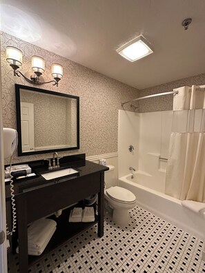 A bathroom with a black vanity, a large mirror, a toilet, and a bathtub with a shower curtain.