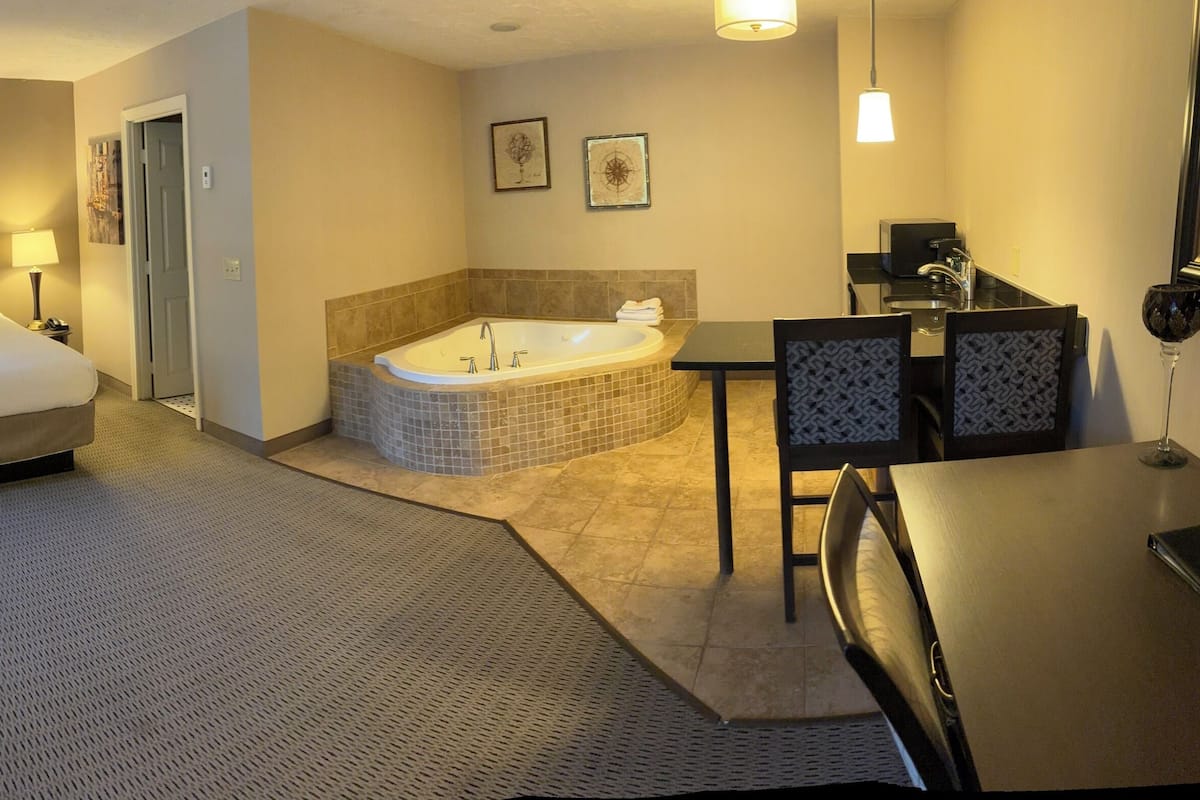 Quarto de hotel com uma cama grande, banheiro privativo com banheira, escrivaninha e uma cadeira.