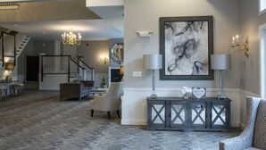 Ein geräumiges Wohnzimmer mit Treppe, einer Chandelüster, einem Konsolentisch mit Dekoration und einem großen abstrakten Gemälde an der Wand.