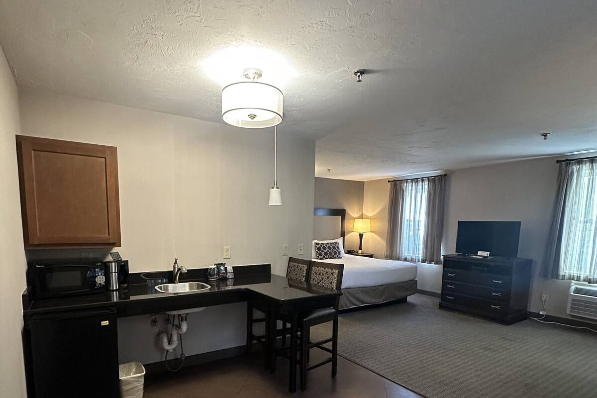 Quarto de hotel compacto com cozinha compacta, cama, televisão e pequeno espaço de estar.
