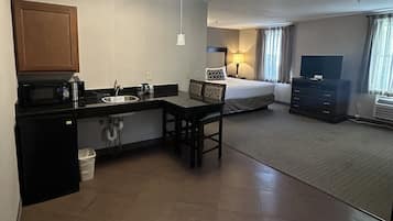 A compact hotel room with a kitchenette, a bed, a TV, and a small seating area.