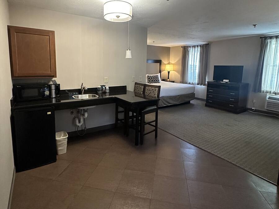 A compact hotel room with a kitchenette, a bed, a TV, and a small seating area.