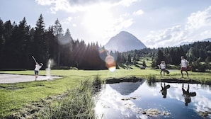 A serene outdoor scene with a mountain in the background, a body of water in the foreground, and a person playing golf. - Alpina (SEEFELD IN TIROL)