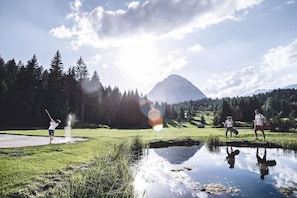Une scène paisible en plein air, avec une montagne en arrière-plan, une étendue d’eau au premier plan et une personne jouant au golf.
