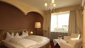 A hotel room with two beds, a sitting area with a table and chair, a chandelier, and a window with curtains. - Alpina (SEEFELD IN TIROL)