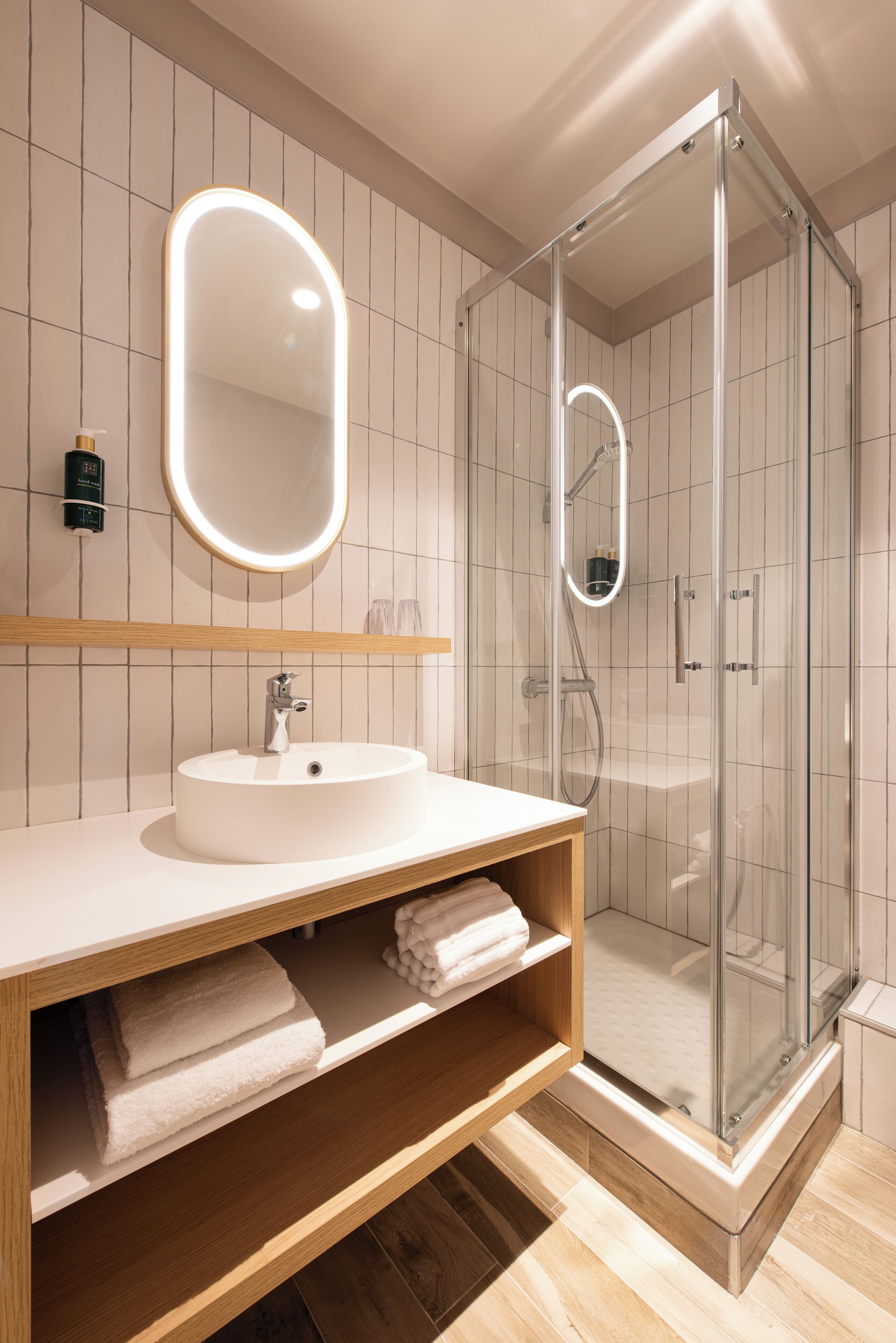 A modern bathroom with a glass-enclosed shower, a round mirror, and a white sink.